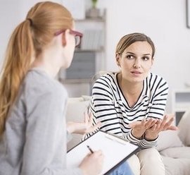 A woman engaged in individual counseling, sitting on a couch and conversing with her therapist.