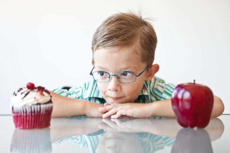 A little boy choosing between a cupcake and apple.
