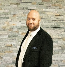 A bald man in a suit standing in front of a stone wall.
