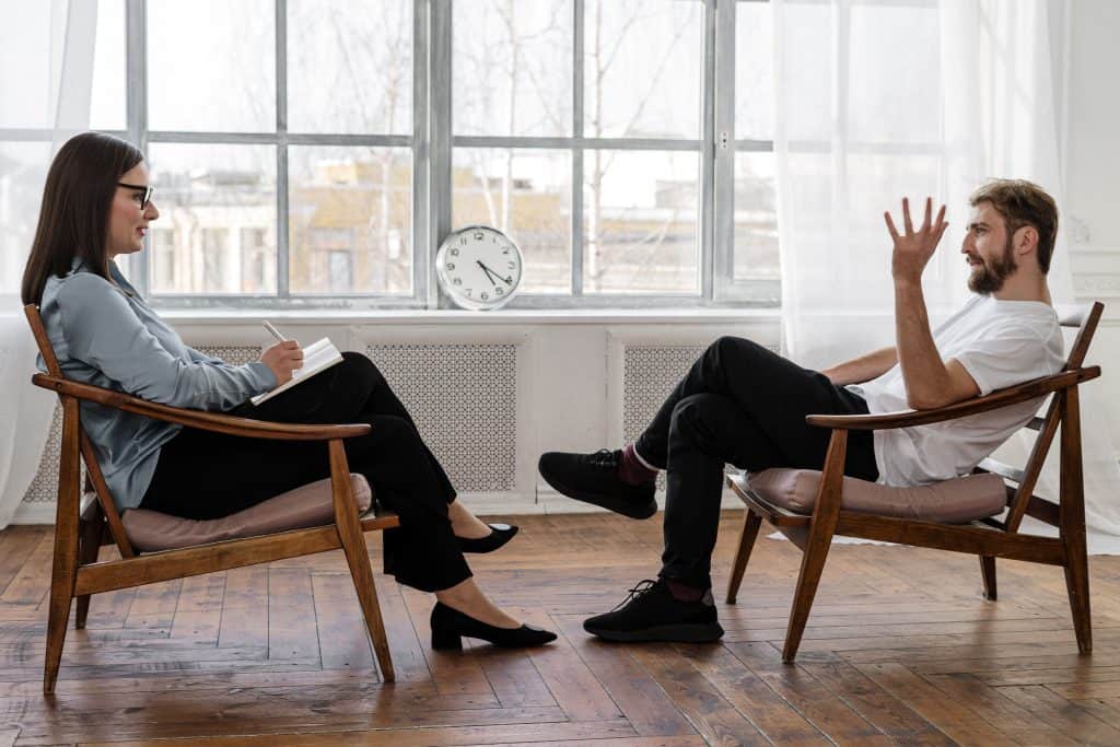 A man and woman engaging in therapy services, sitting in chairs and talking to each other for mental health support in Overland Park, Kansas City KS.