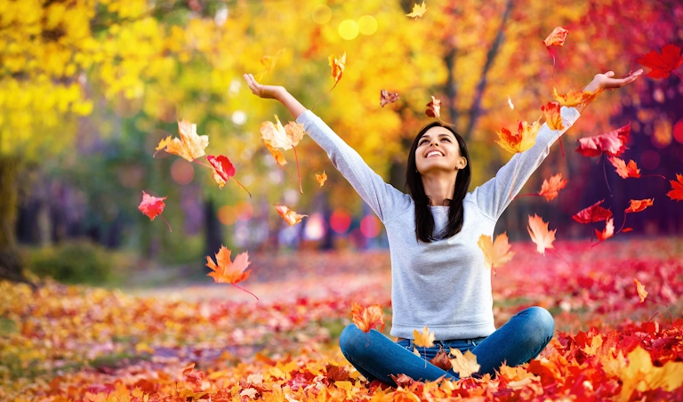 A happy woman plays in fall leaves, boosting her mental health