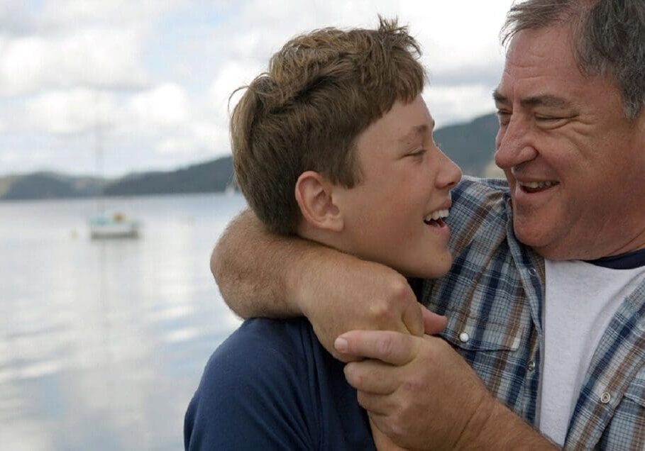A man and boy are hugging near the water.